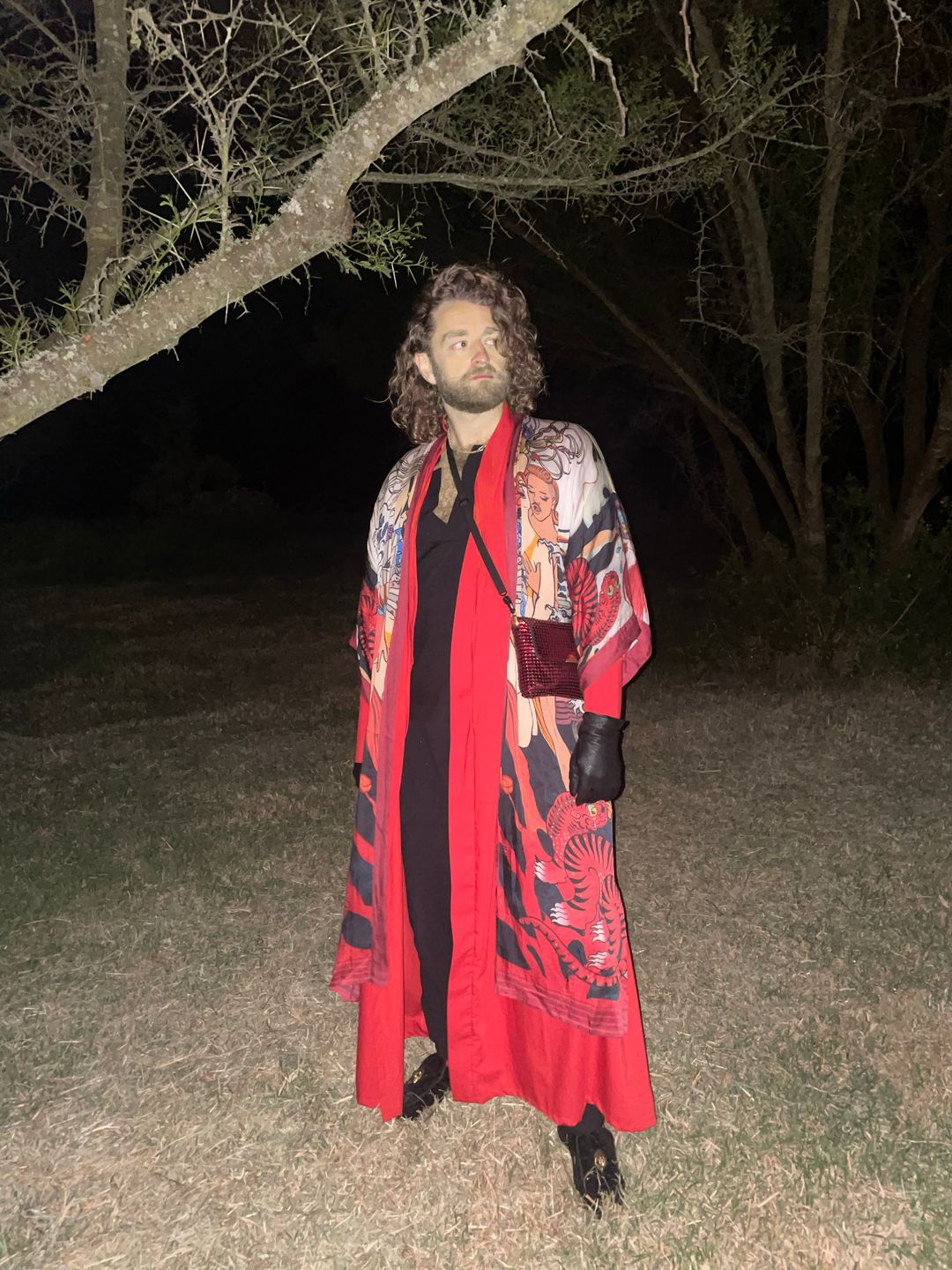 Björgvin at night in a long red patterned robe, standing beneath a tree.
